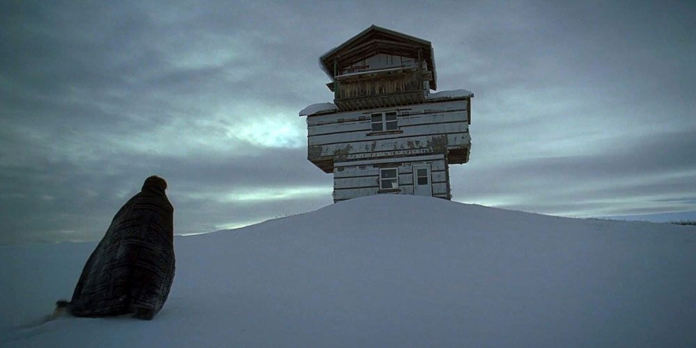 A figure looks at the building in the snow in The Lodge