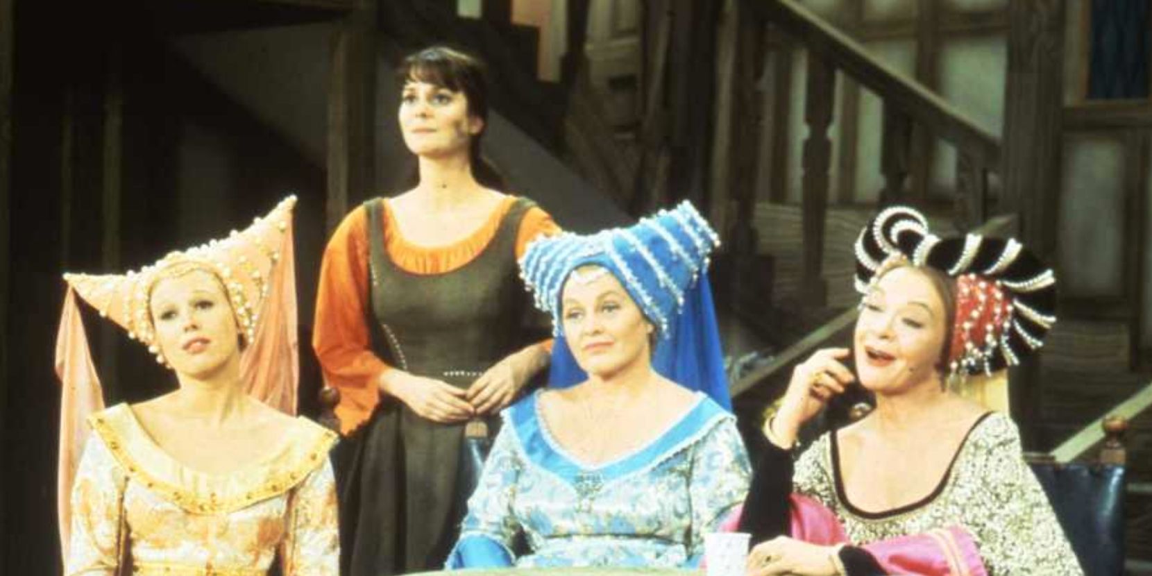Cinderella stands behind her seated stepsisters and stepmother in Rodgers and Hammerstein 1965 Cinderella