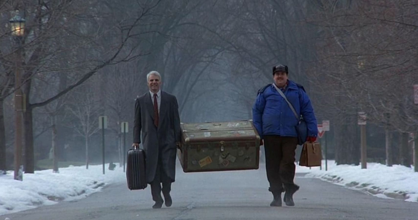 Del and Neal carrying Del's trunk in street in Planes, Trains and Automobiles