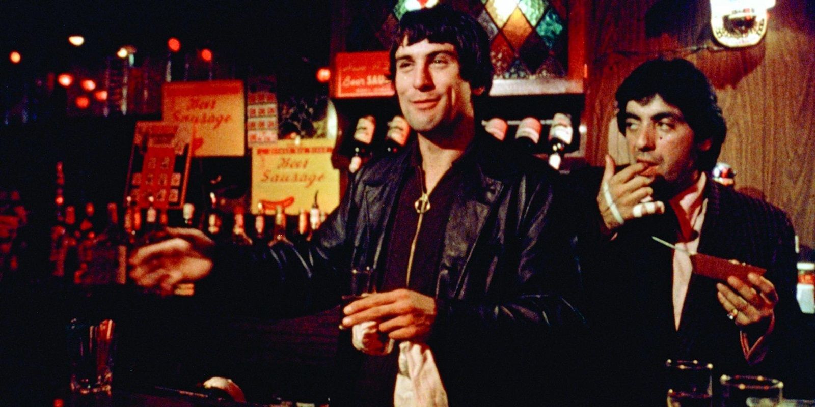 Robert De Niro sorrindo e parado perto de um balcão de bar em Mean Streets, de Martin Scorsese