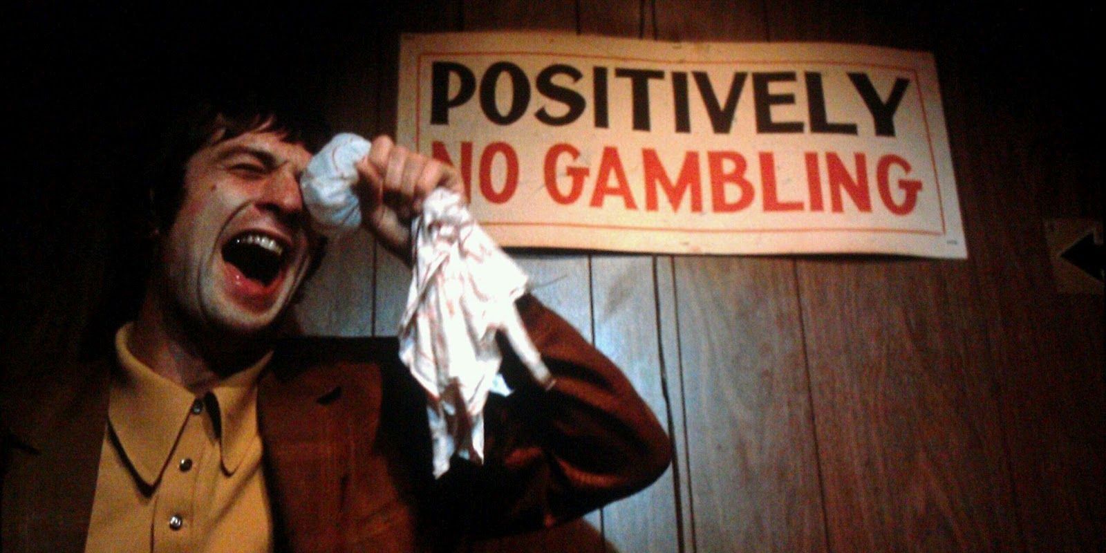 Robert De Niro laughs with a No Gambling sign behind him in Mean Streets