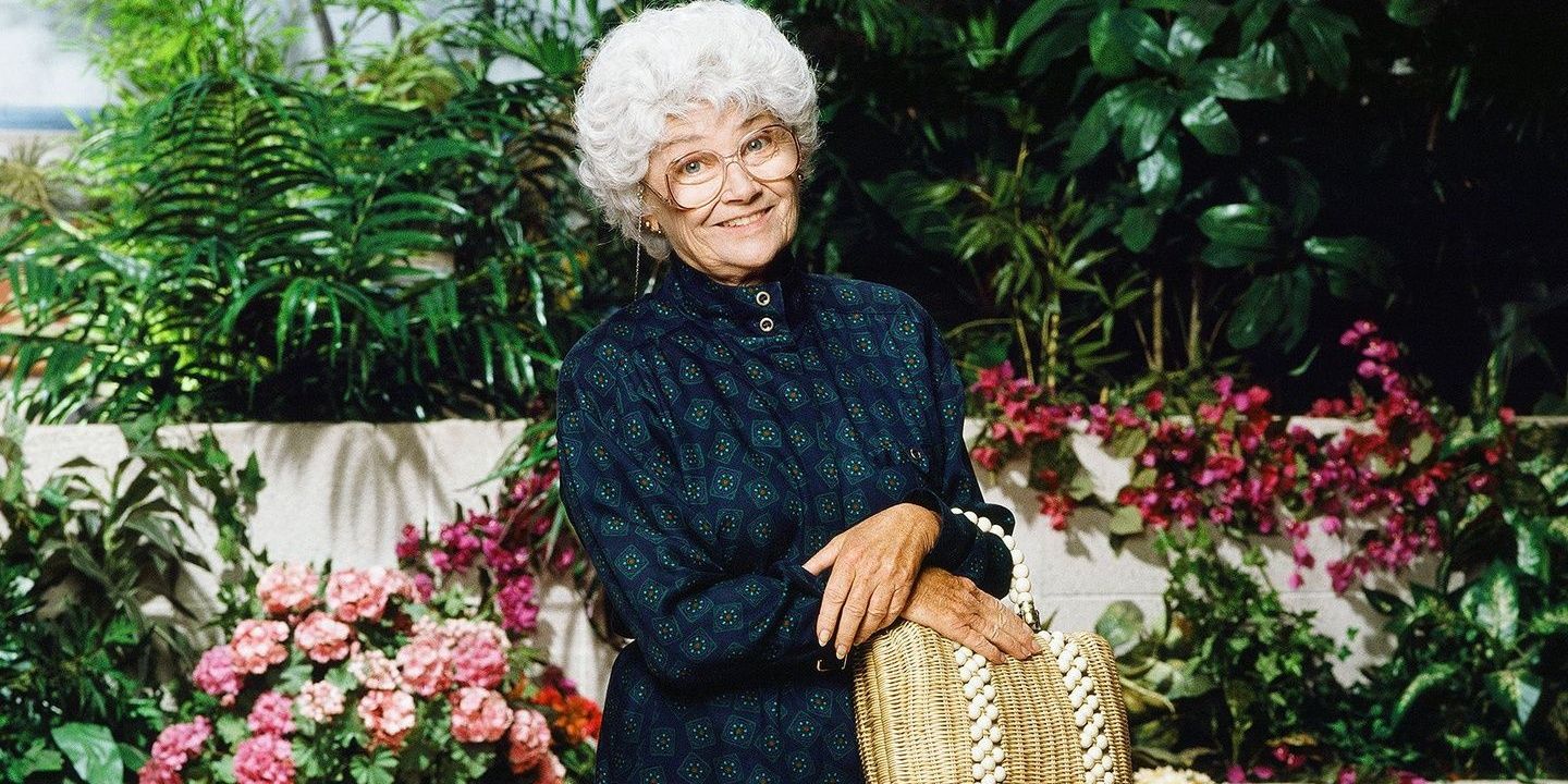 Sophia Petrillo holds a bag in front of flowers in a promotional image for The Golden Girls 
