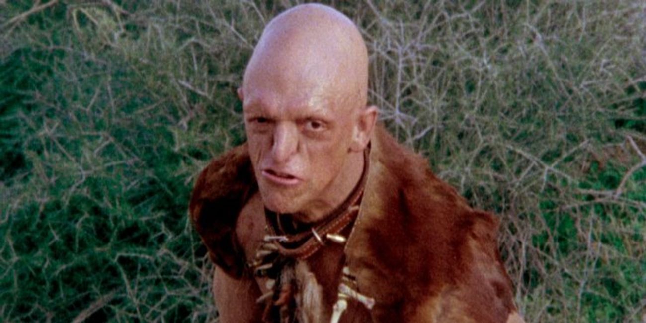 A bald man grimaces in a grassy field in The Hills Have Eyes.