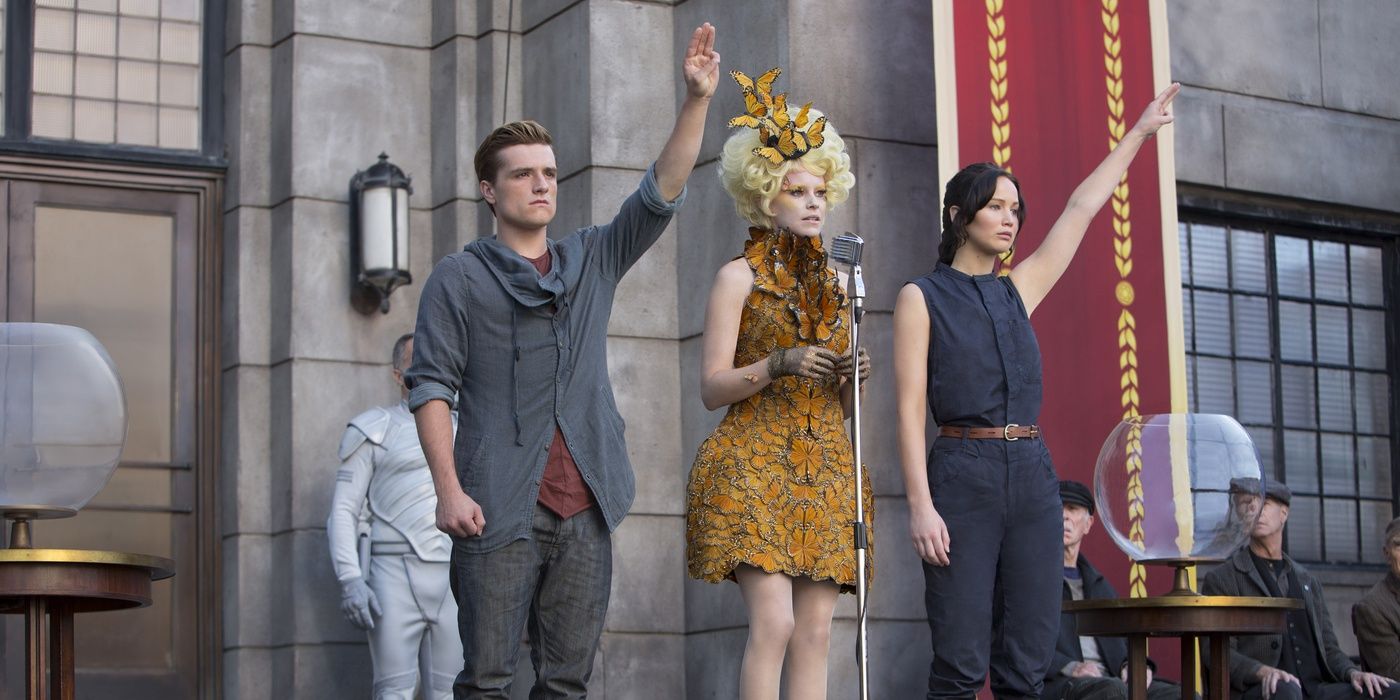 Josh Hutcherson as Peeta, Elizabeth Banks as Effie Trinket, and Jennifer Lawrence as Katniss Everdeen holding their hands up in The Hunger Games: Catching Fire