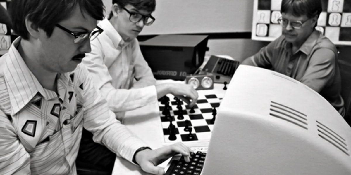 Two characters playing chess and one on the computer in black and white image from Computer Chess documentary 2013