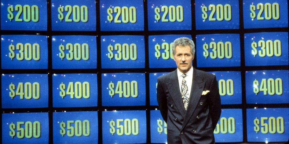 Alex Trebek in front of a Jeopardy screen
