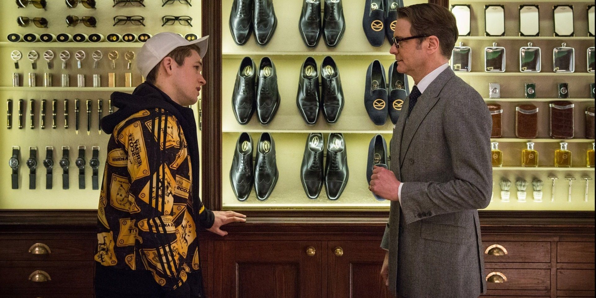 Colin Firth e Taron Egerton conversando em frente a uma vitrine de sapatos em Kingsman The Secret Service