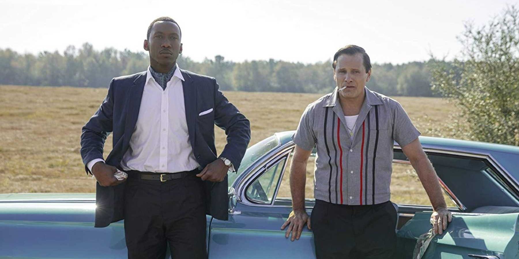 Two men stand next to a blue car outside in Green Book.