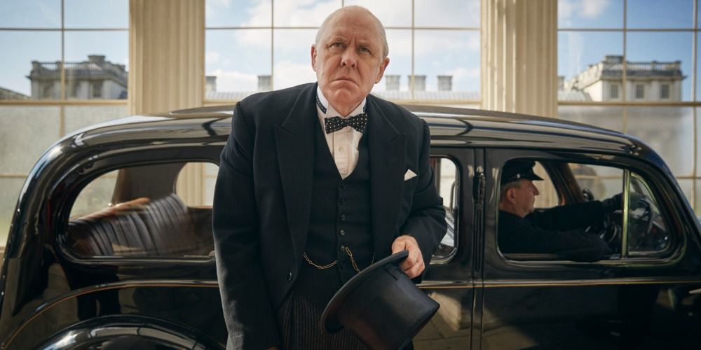 An image of John Lithgow in The Crown. He is seen to be wearing a black tuxedo and getting out of a black service car