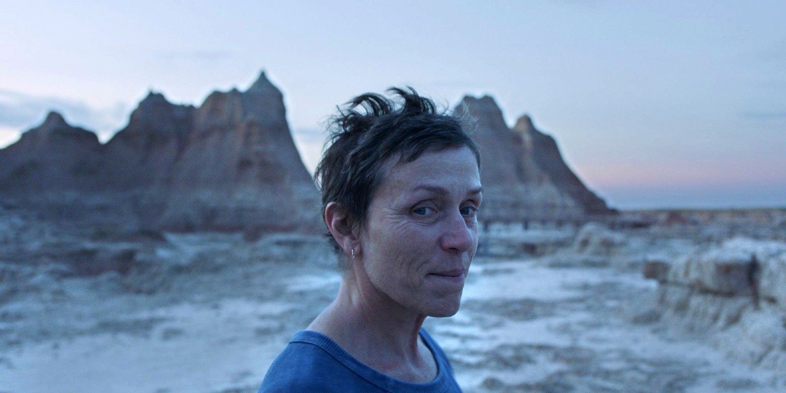 Frances McDormand in Nomadland smiling with mountain range in the background 