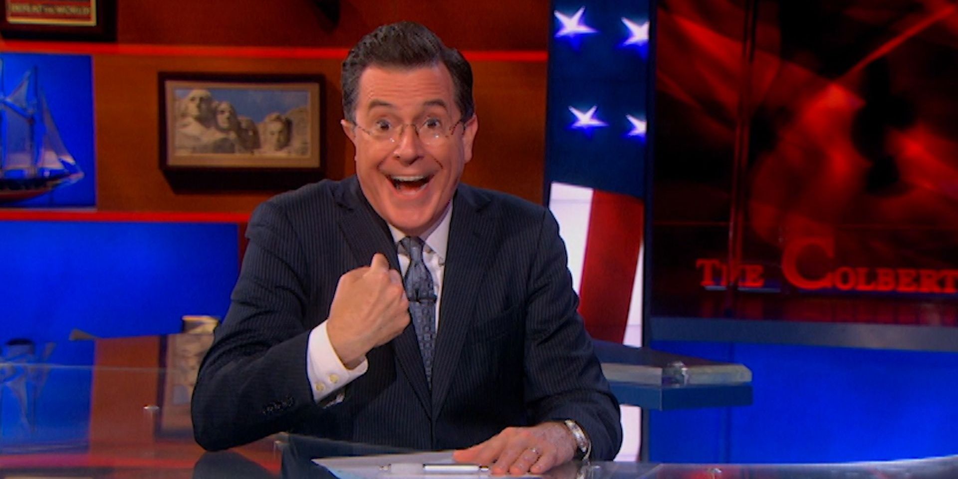 Stephen Colbert sits behind his desk in The Colbert Report.