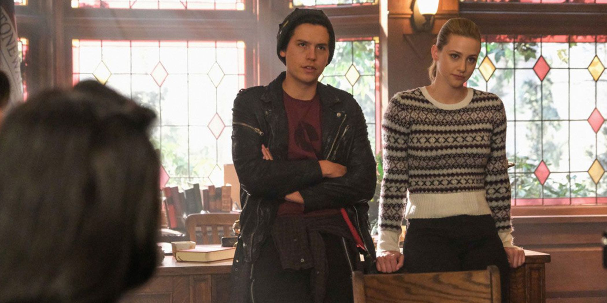 Jughead, arms crossed, next to Betty on desk in Stonewall Prep classroom