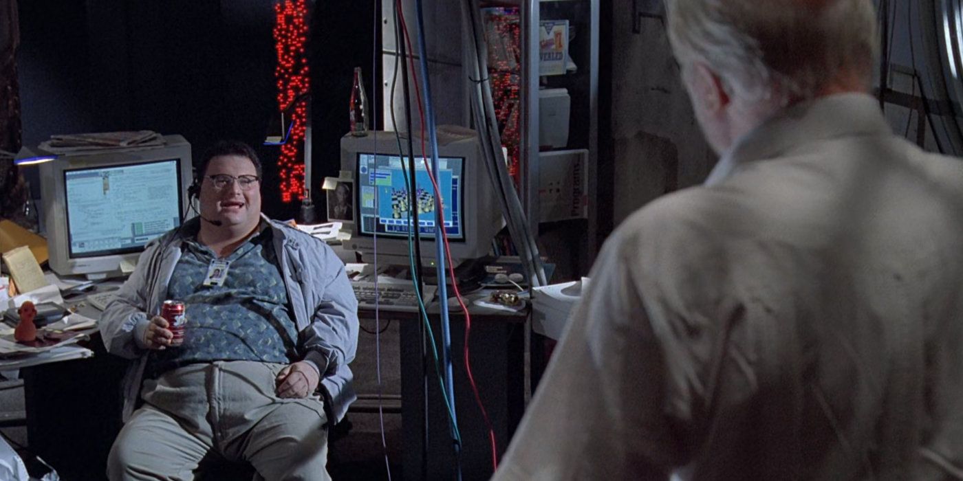 Nedry sitting in a chair arguing with John Hammond who has his back to the camera