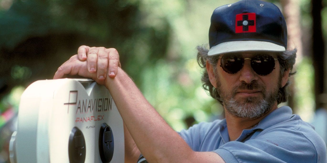 Steven Spielberg leaning against his camera wearing shades and a cap