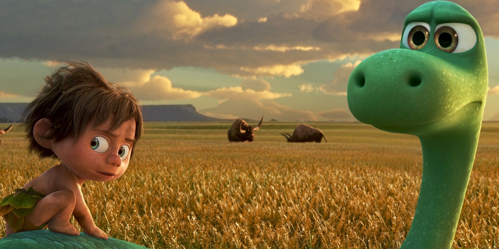 Arlo and Spot in a sunny field look behind them in The Good Dinosaur.
