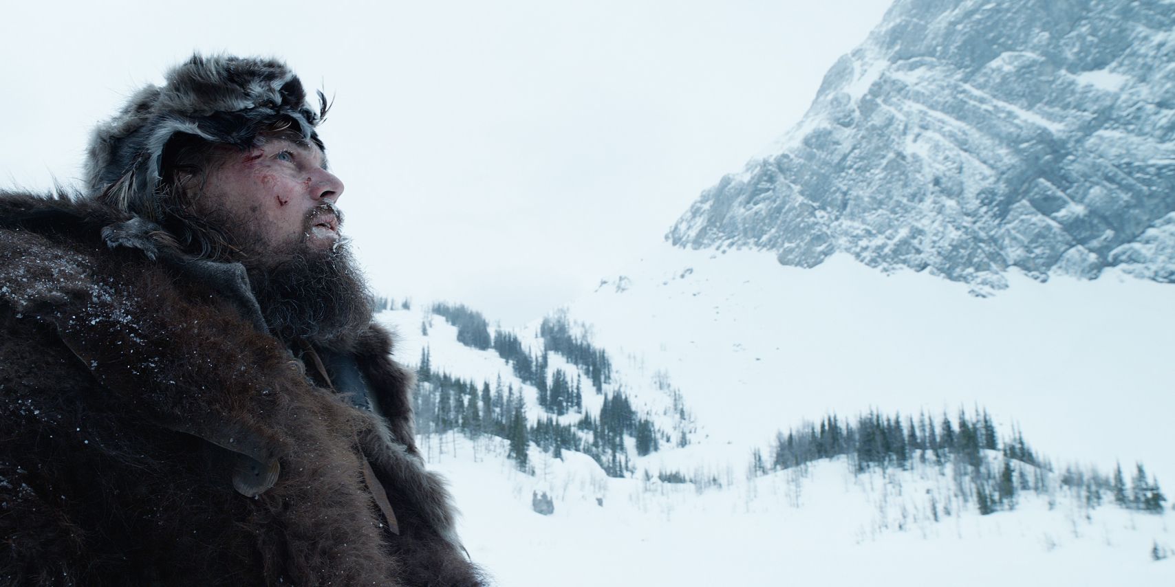 Leonardo Dicaprio looks at the sky with a snowy mountain in the background in The Revenant.
