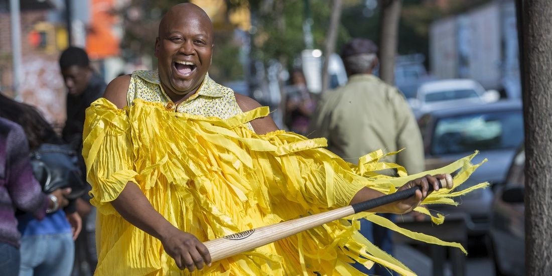 Titus grins while wearing a bright yellow dress and performing Lemonade in Unbreakable Kimmy Schmidt