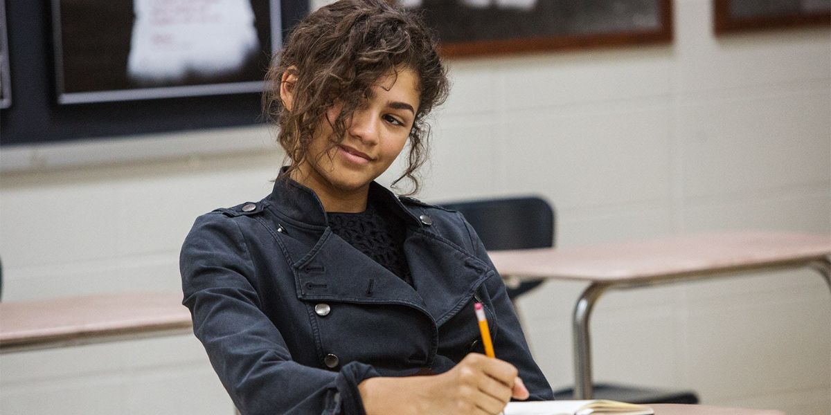 Zendaya as MJ in Spider-Man: Homecoming, sitting at a school desk, writing in notebook with a pencil