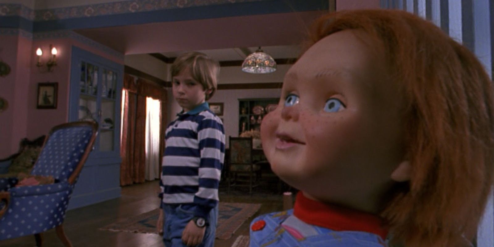 Chucky sitting in a chair while Andy looks over Child's Play 2