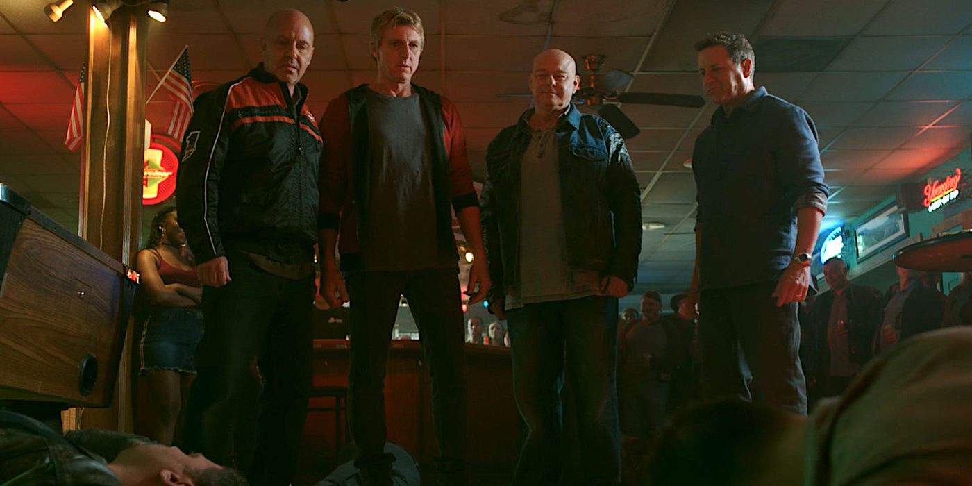 Johnny com Bobby, Tommy e Jimmy em um bar, olhando para homens espancados após uma briga em uma cena de Cobra Kai
