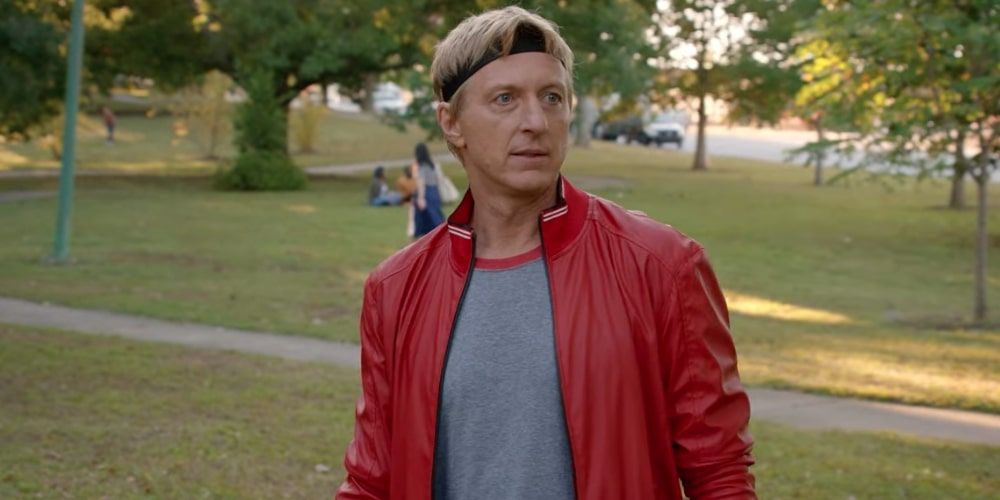 Johnny in a red jacket and headband in the park in Cobra Kai