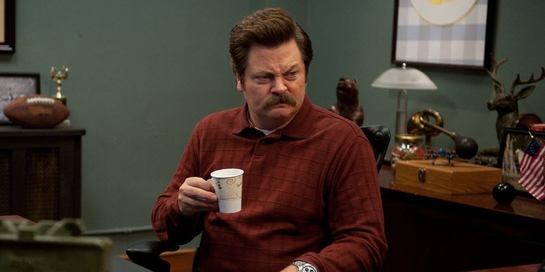 Ron Swanson (Nick Offerman) sitting behind desk with coffee mug