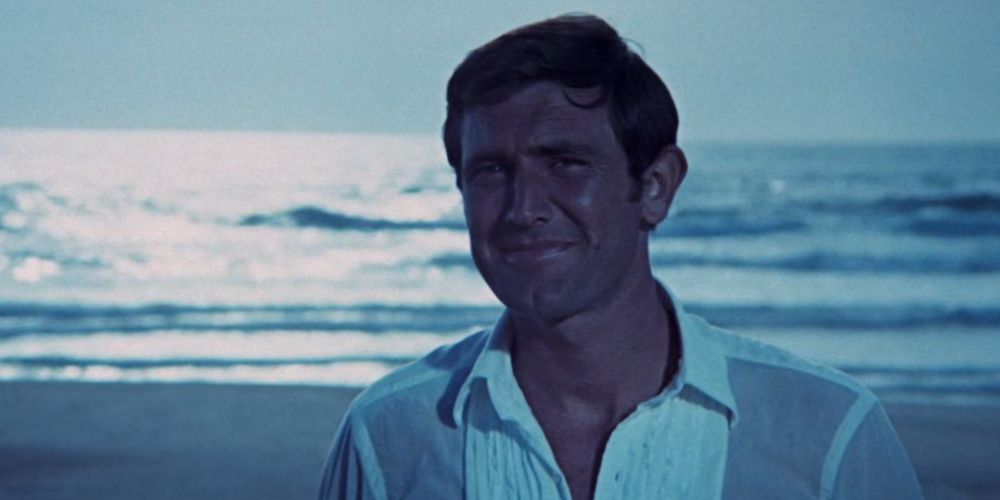 George Lazenby as 007 standing on the beach