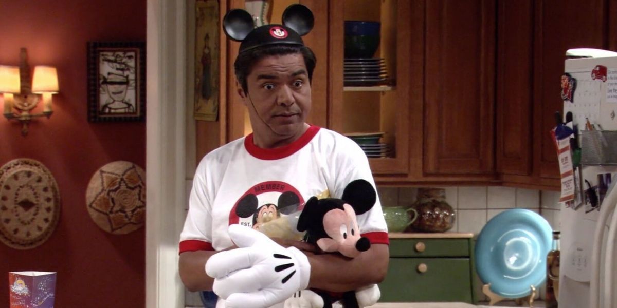 George Lopez in a mickey hat and mickey shirt holding a mickey stuffed animal. 