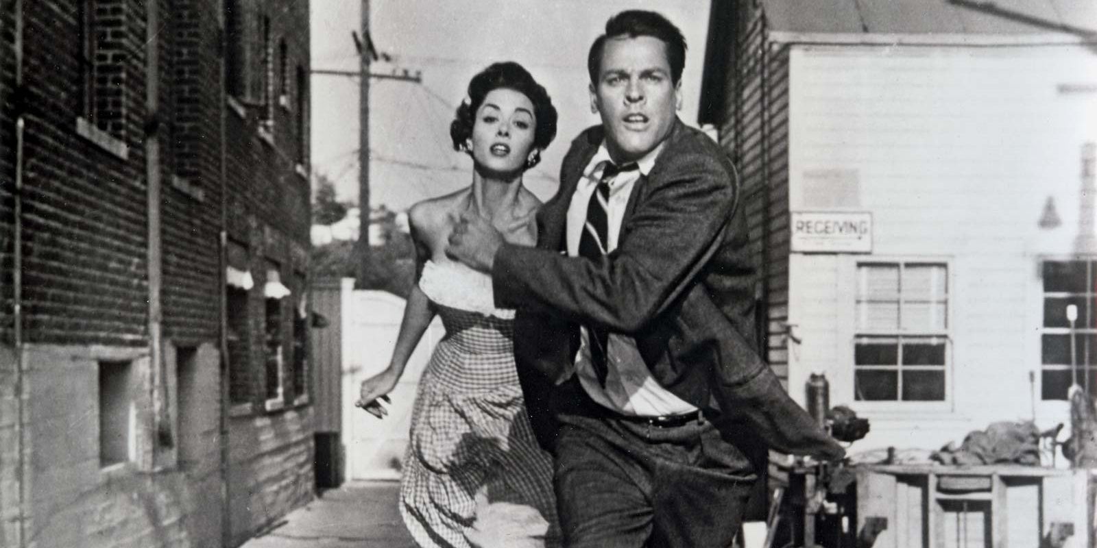 Um homem e uma mulher correm por uma rua em Invasion of the Body Snatchers.