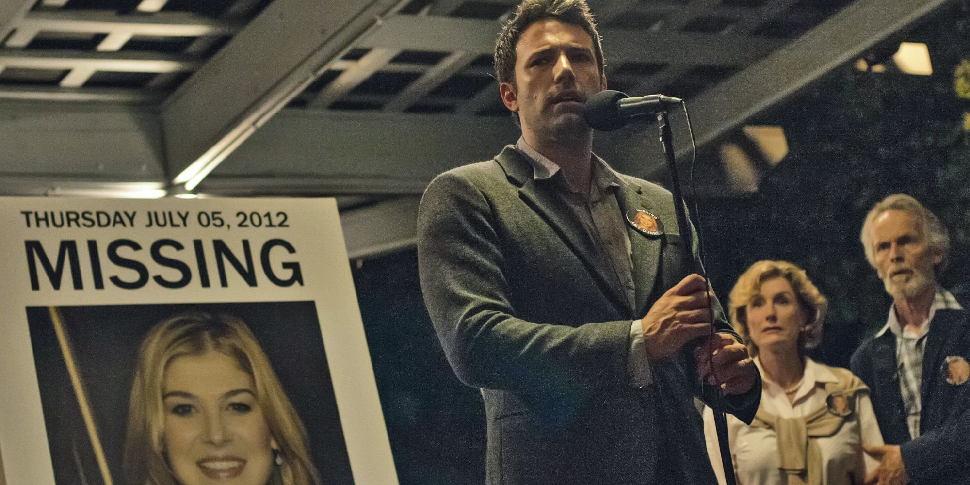 Nick addresses a crowd with a picture of his missing wife behind him in Gone Girl