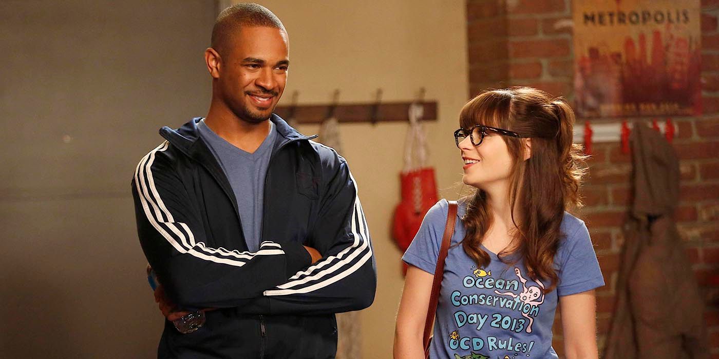 Jess y Coach parados uno al lado del otro y sonriendo en New Girl