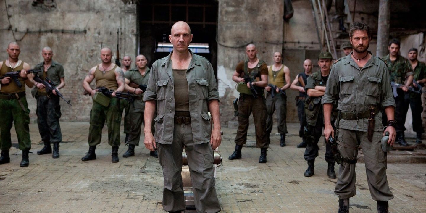 Ralph Fiennes in stands in yard with armed soldiers in Coriolanus