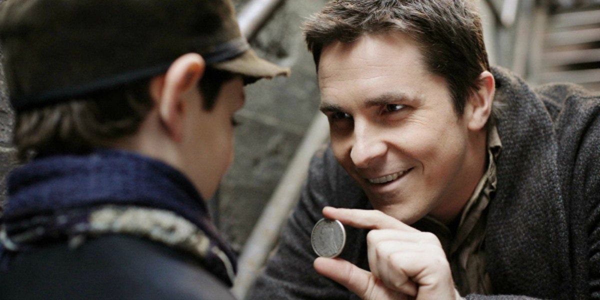 Christian Bale holding a coin up to a boy in The Prestige