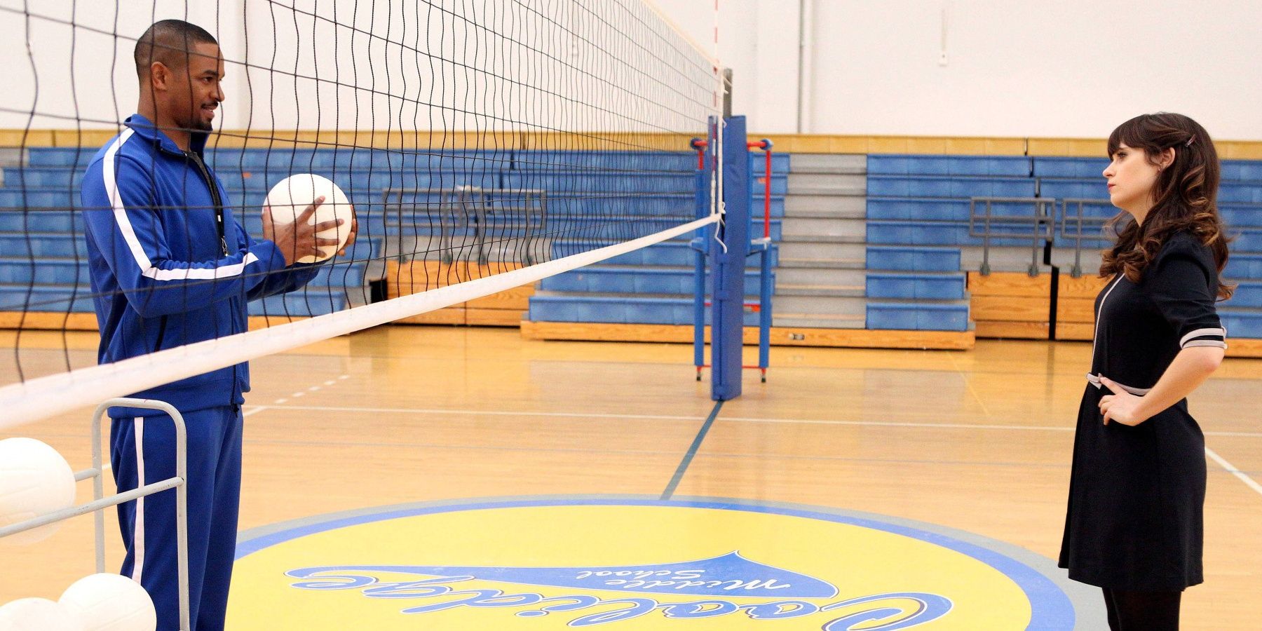 Coach holds a volleyball while Jess stands on the other side of the net