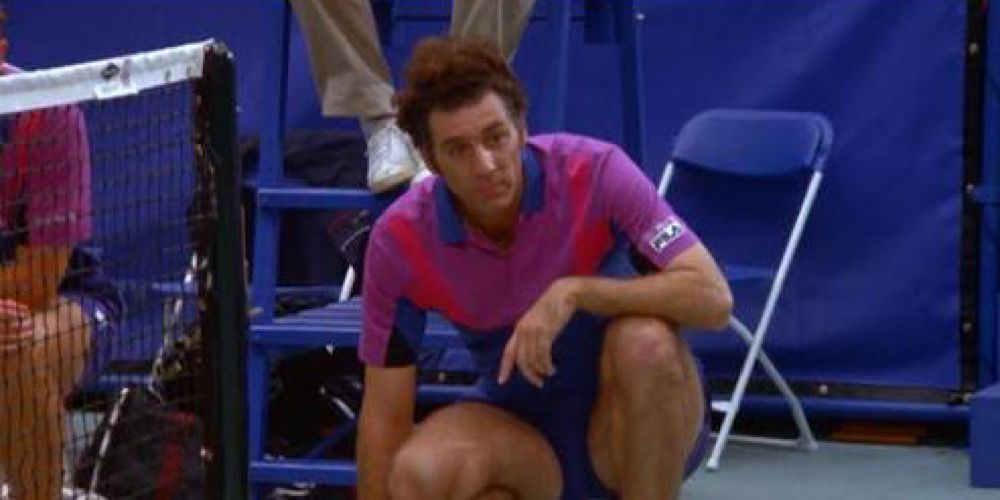 Kramer kneels at the edge of a tennis court waiting to retrieve the ball