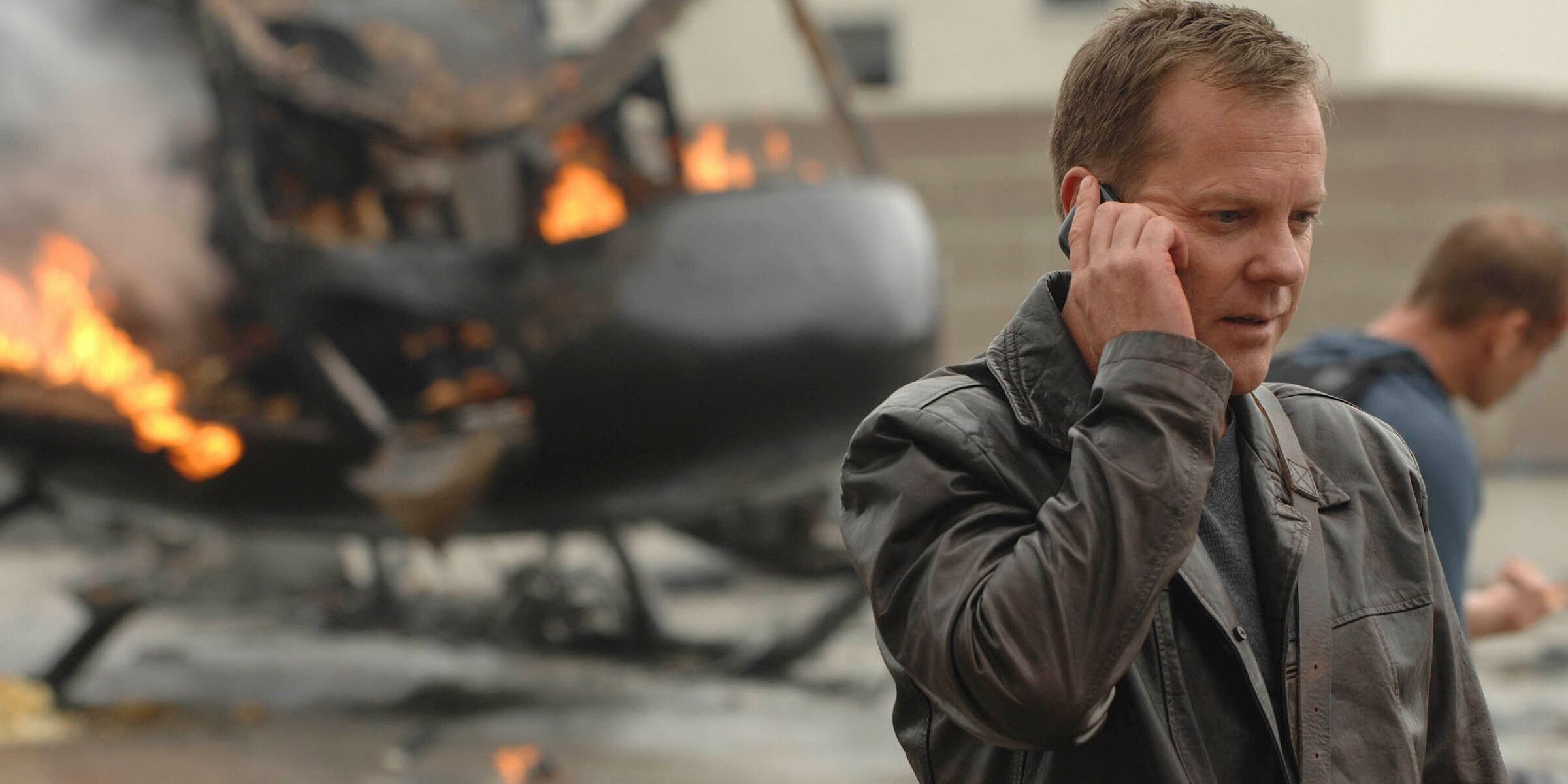 Jack Bauer on the phone while a chopper burns in the background in 24
