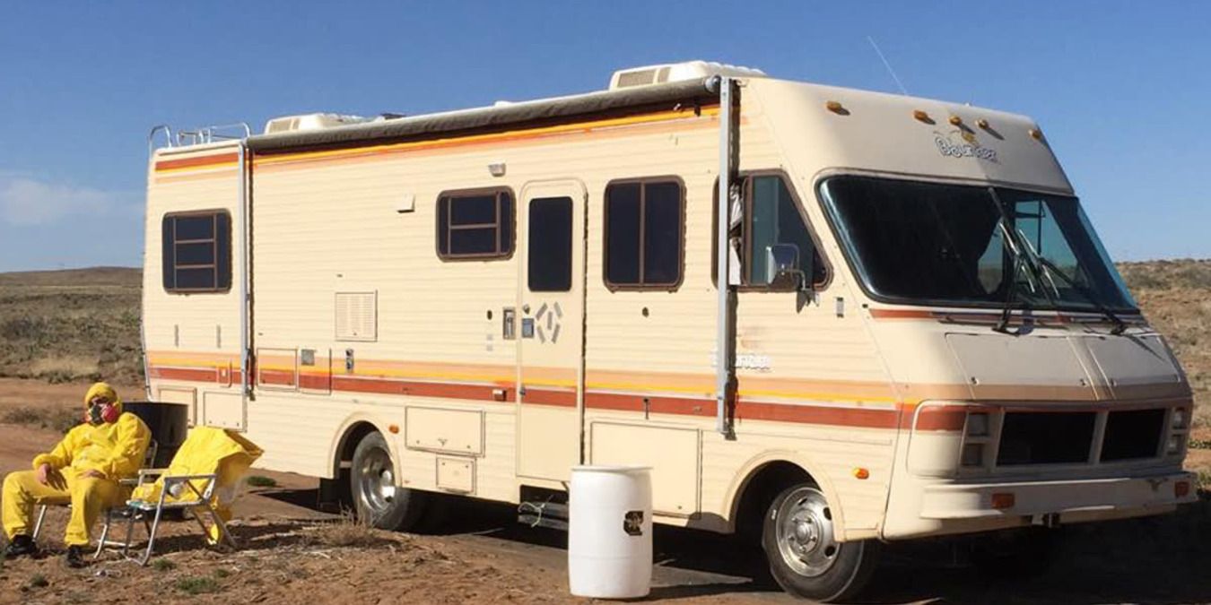 Scene from Breaking Bad with Walter White sitting outside the RV in the desert, wearing his yellow lab suit