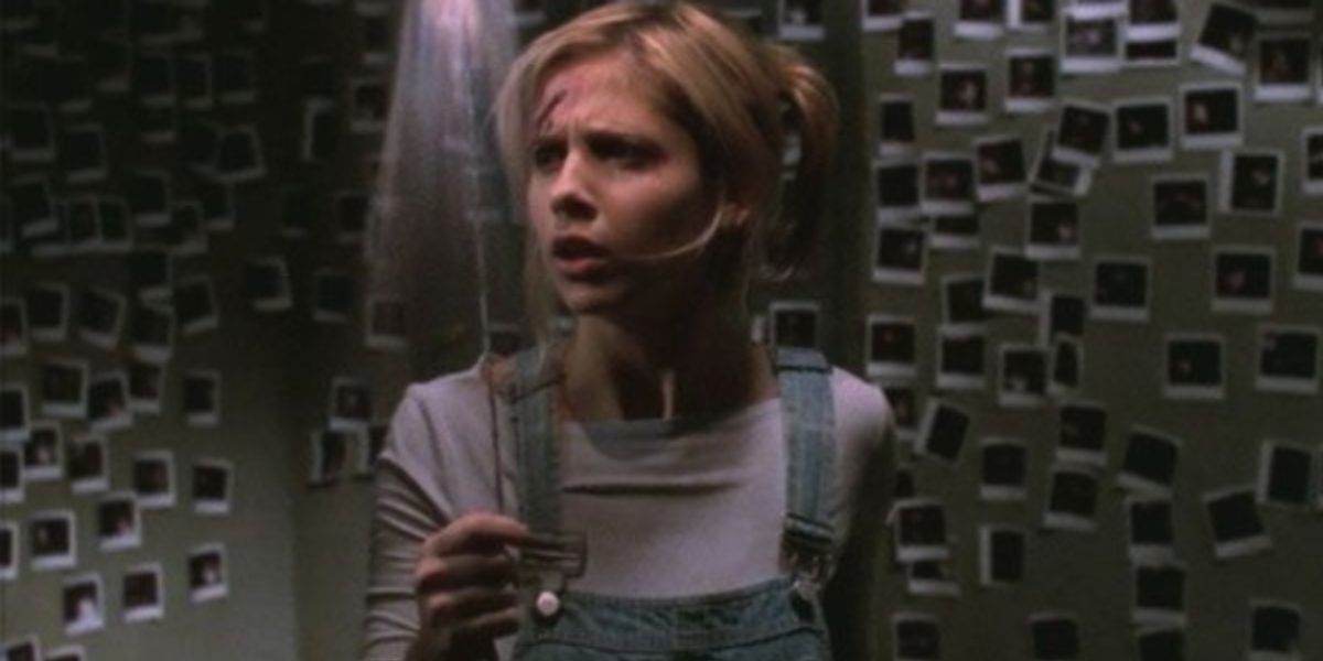 An image of Buffy locked in a room by herself. She is wearing blue dungarees and a grey shirt. She looks confused as she notices that there are numerous polaroids on the walls, which are shown in the background of the images 