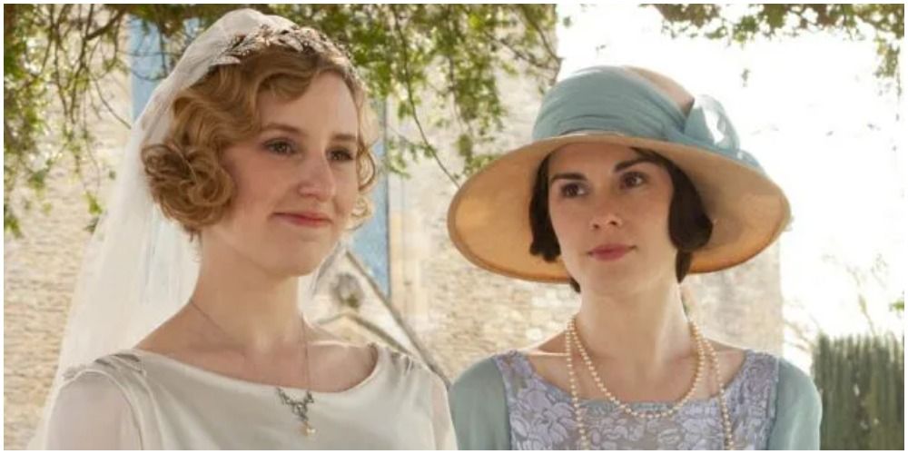 Bride Edith standing next to Mary in a blue dress and bonnet in Downton Abbey