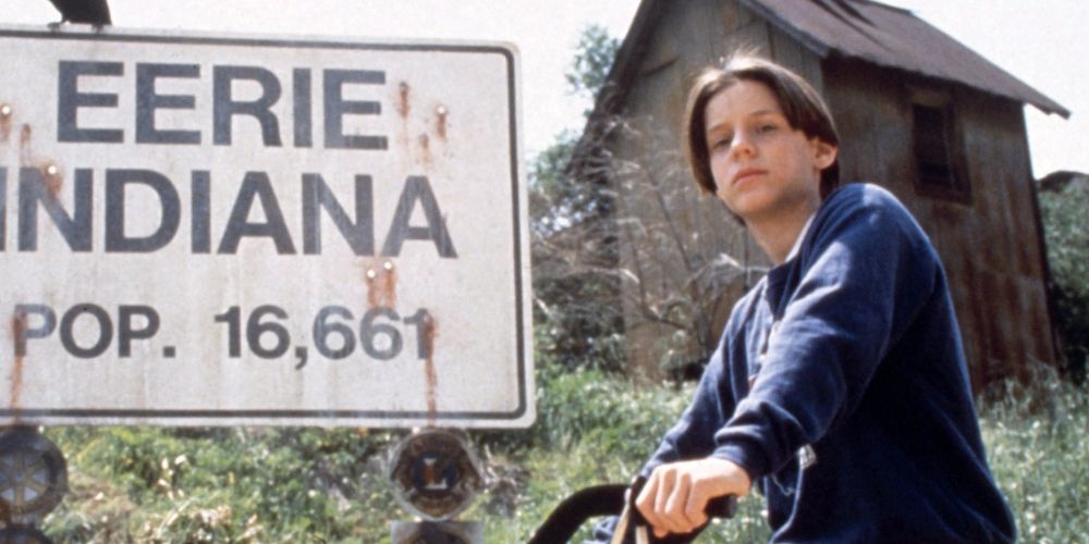 Marshall Teller riding his back past the welcome sign for Eerie, Indiana