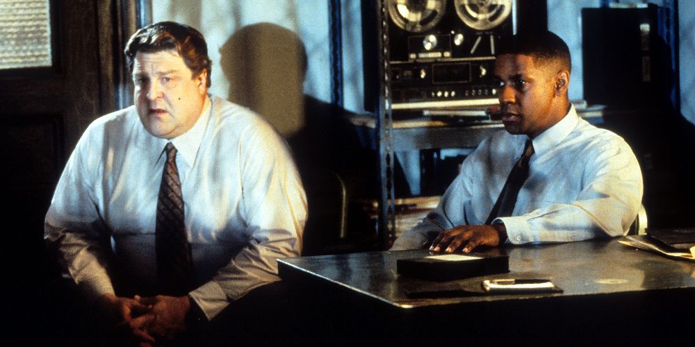 John Goodman e Denzel Washington seduti in una stanza scarsamente illuminata in Fallen