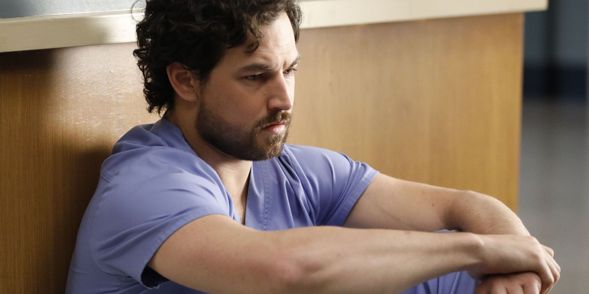 Animage of DeLuca sitting on the floor in the hospital lobby in Grey's Anatomy