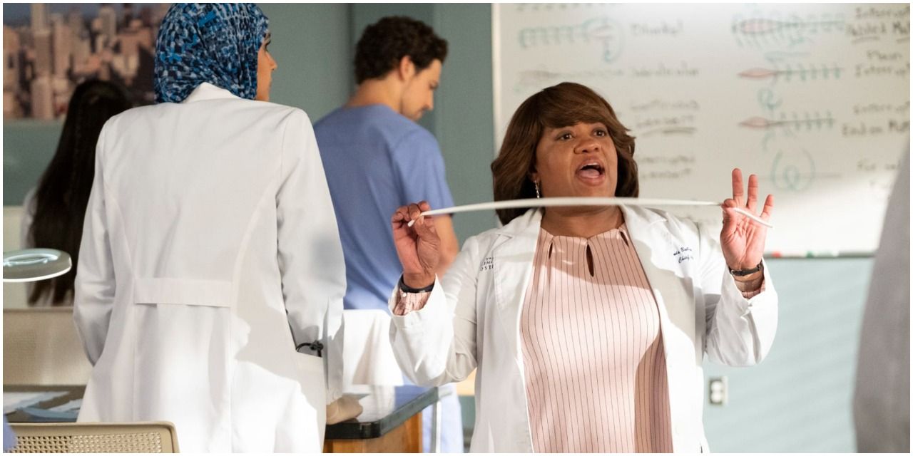 An image in Miranda Bailey in Grey&rsquo;s Anatomy. She appears to be wearing a white dress as well as a white labs coat, and holding a tape measure. Behind her, there are interns standing and listening to her