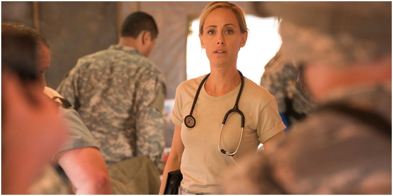 An image of Teddy Altman in Grey&rsquo;s Anatomy. She is wearing a beige top, has a stethoscope around her neck and is surrounded by army soldiers