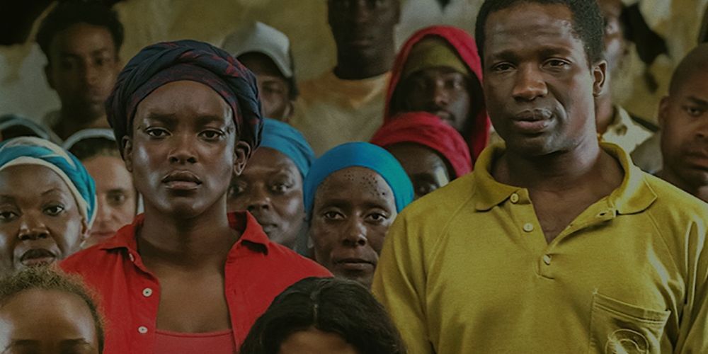 Wunmi Mosaku and Sope Dirisu's characters from His House looking straight into the camera with other refugees around them