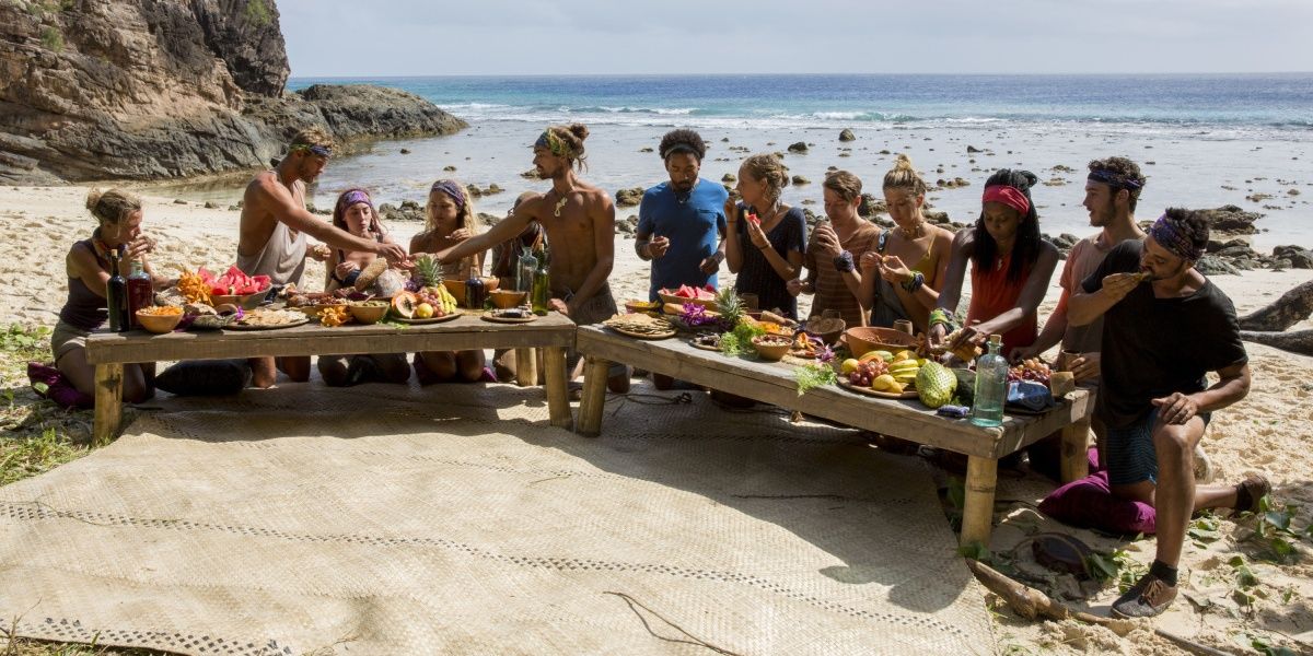 Survivor contestants sit around a table and eat