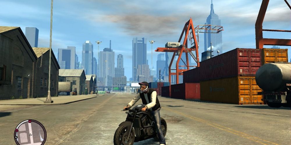 Luis sits on a black motorbike at the docks in front of shipping containers in GTA: The Ballad of Gay Tony