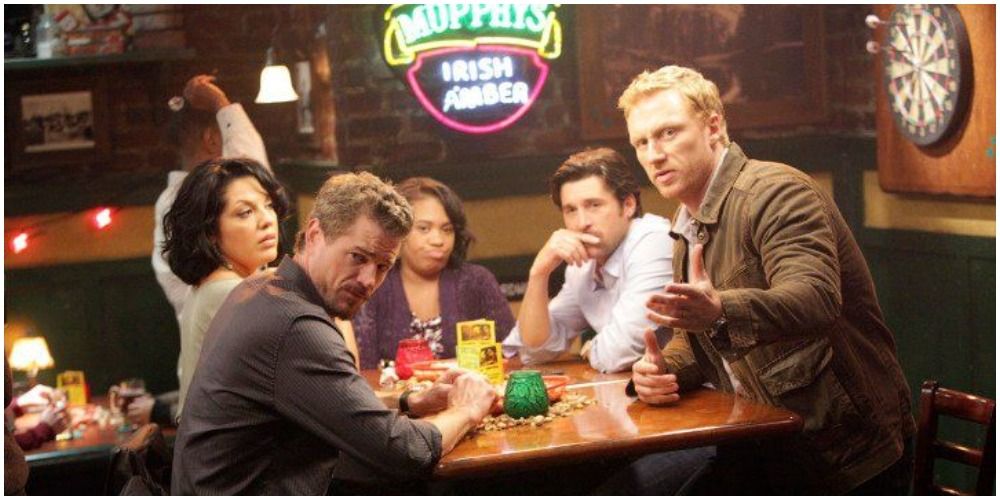 An image of Mark, Callie, Bailey, Derek, and Owen all sitting around a table in Joe's bar. They seem to have been drinking based on the drinks on the table and looking at what Owen is pointing at off-screen