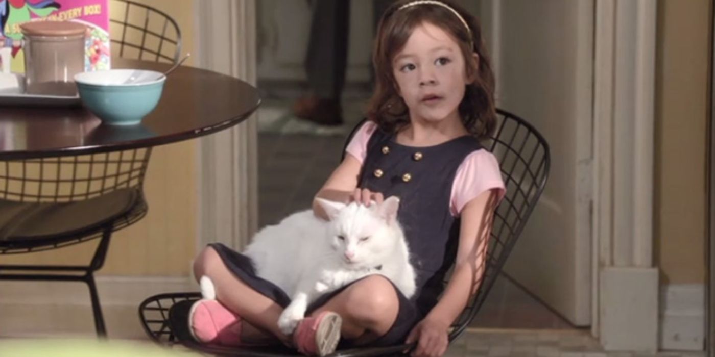 Lily in Modern Family as a toddler, sitting on a chair, stroking a cat.