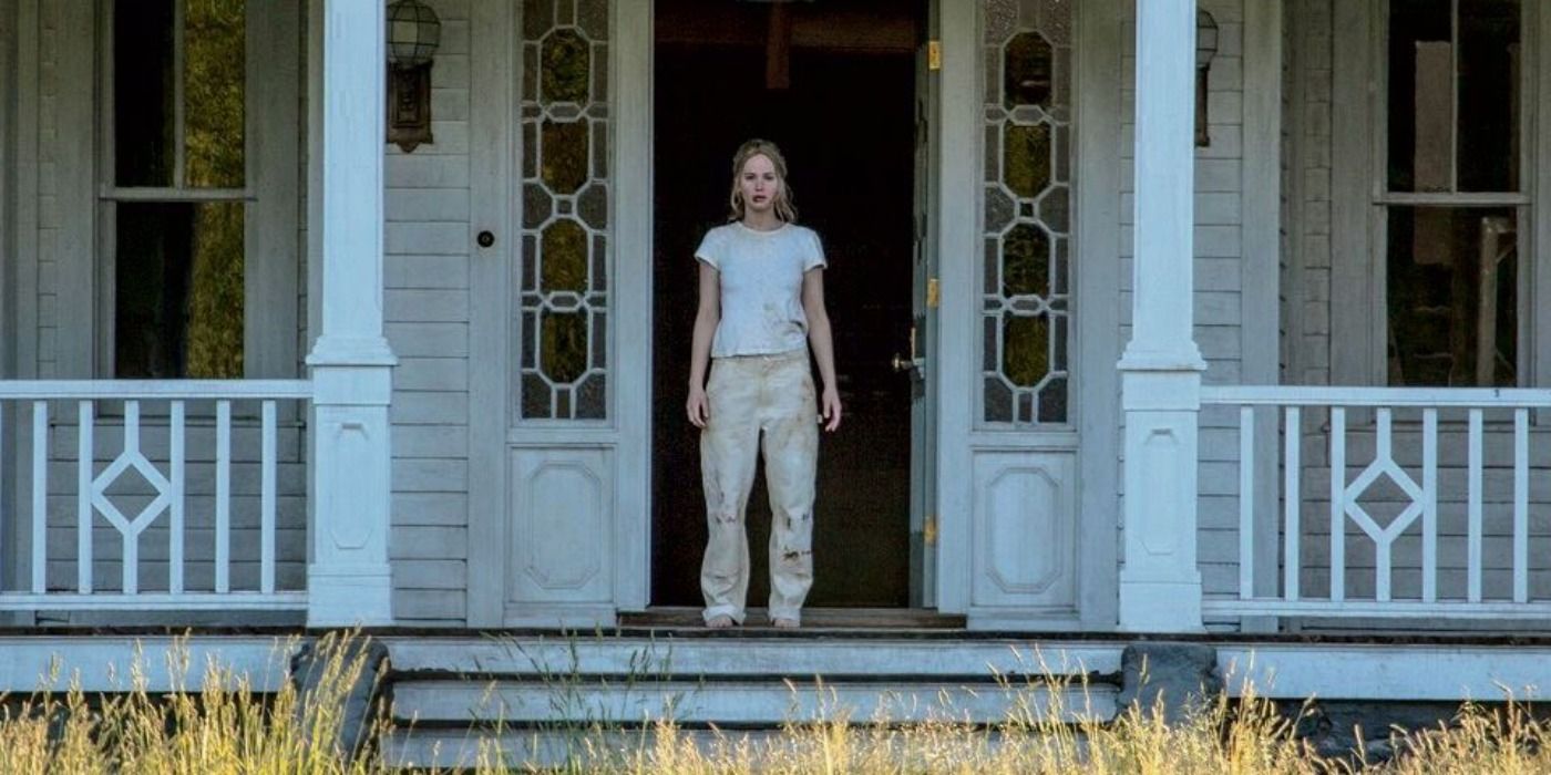 Jennifer Lawrence's mother character wearing paint clothes, standing on porch on a sunny day with door open